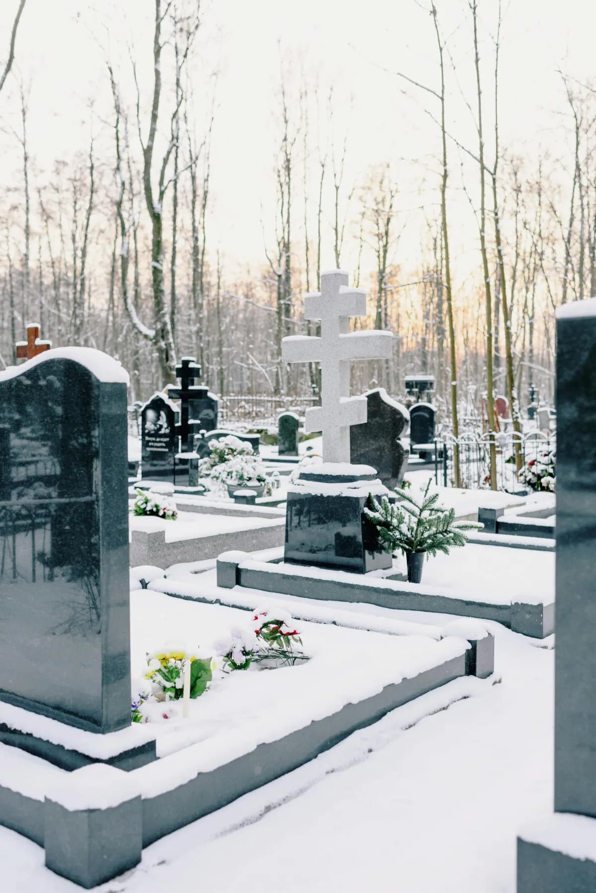 Заснеженное кладбище с гранитными памятниками и крестом